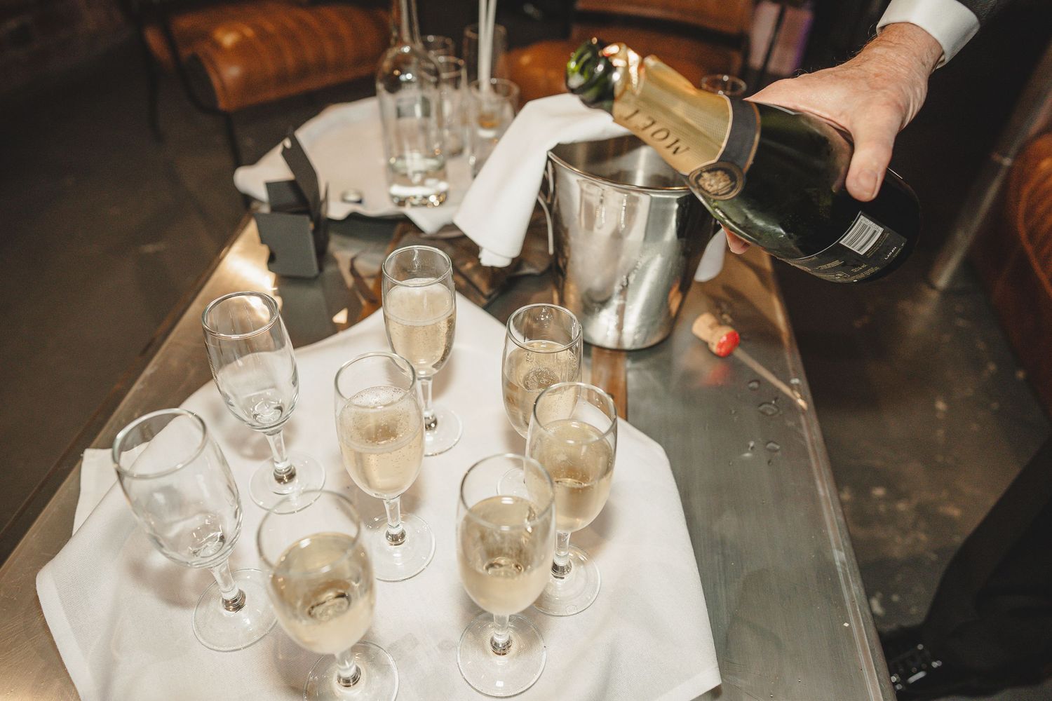 Several hands reach for wine glasses on a table during a celebratory toast at a social gathering.
