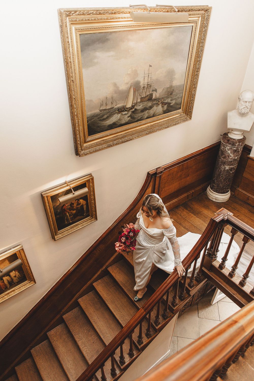 A series of vintage framed nautical paintings line the wall along a wooden staircase in a classic interior setting.