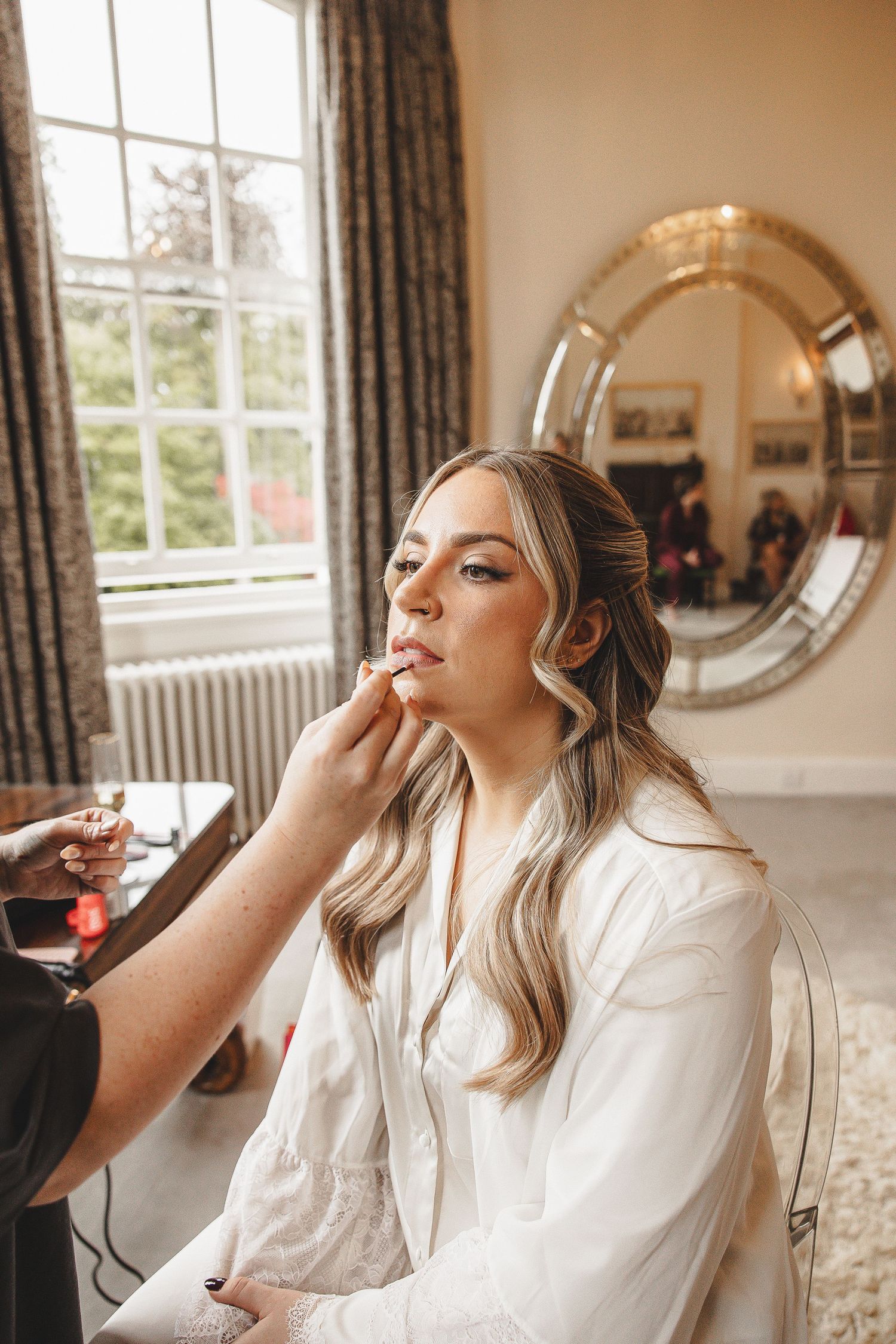 Series of photos showing someone getting their makeup professionally applied in an elegant room with large windows.