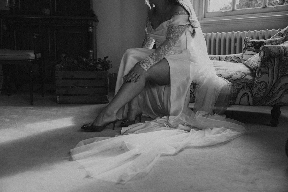 A vintage black and white photograph showing someone in an elegant dress sitting on a chair with dramatic lighting.