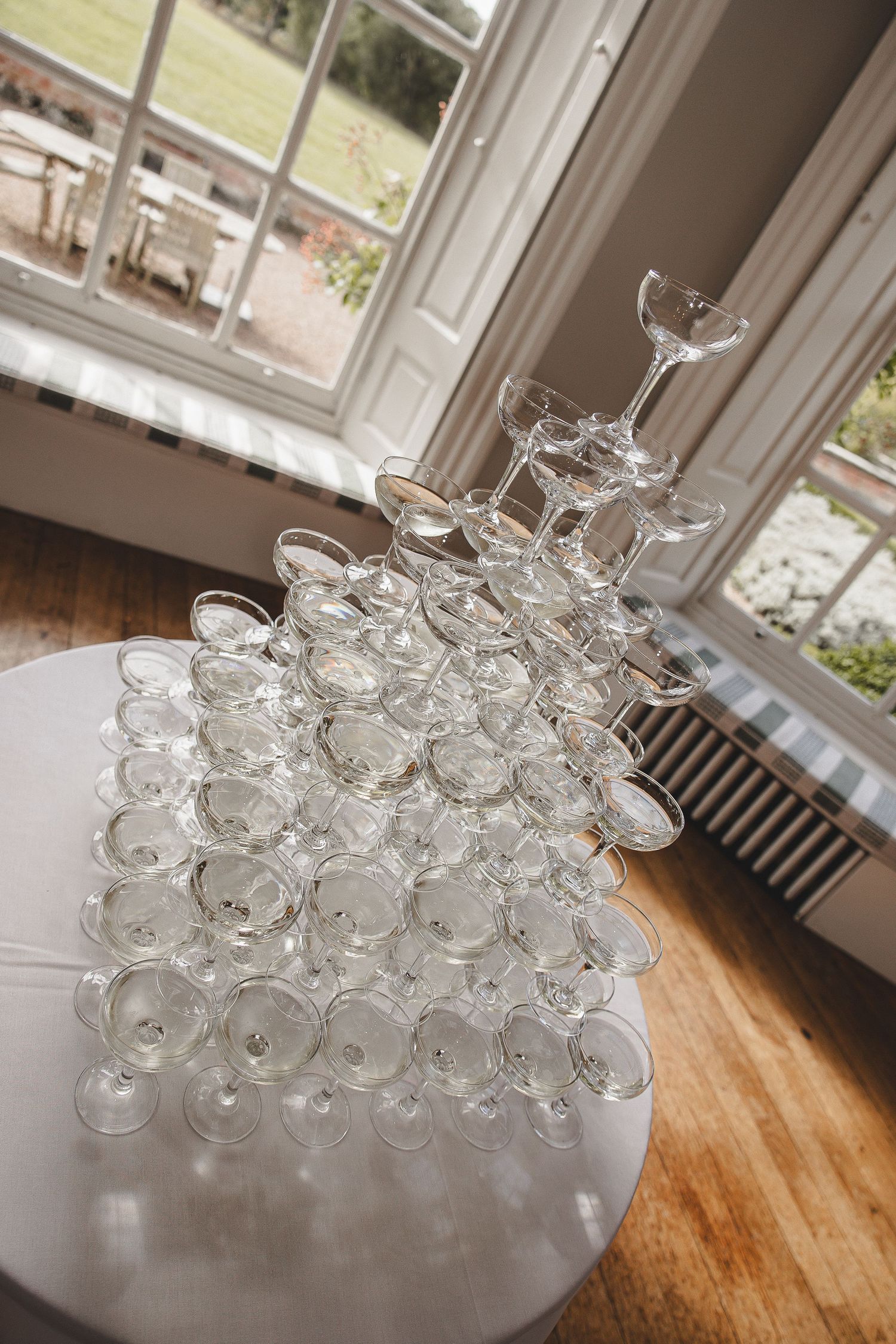 Multiple clear glass martini cocktail glasses arranged in neat rows on a wooden surface near a bright window.