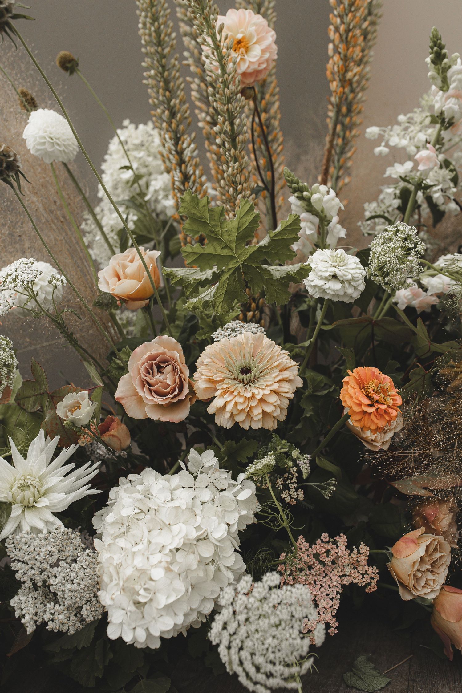 Romantic floral arrangement with peach roses, white hydrangeas, and dried wheat stems in muted earth tones.