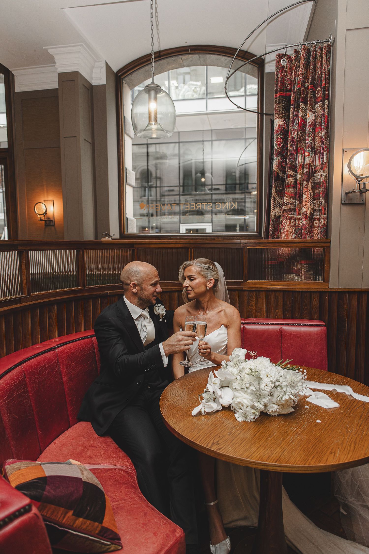 A couple shares an intimate moment at a restaurant booth with red leather seating and wooden tables.