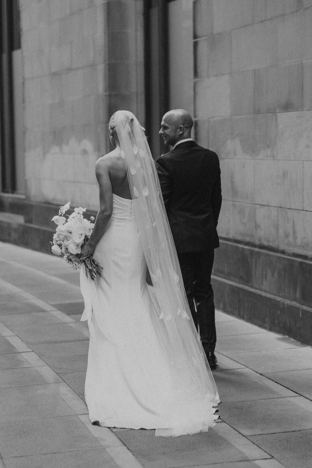 A black and white sequence of a bride and groom walking away from camera showing the flowing veil and wedding dress.