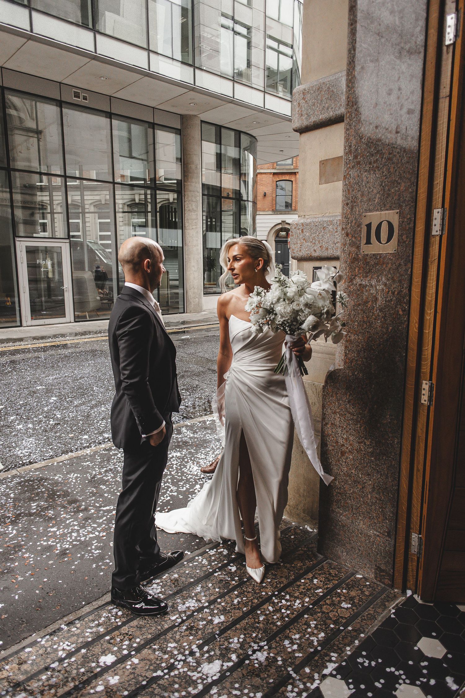 A wedding couple enters a building with white flower petals scattered on the ground in a series of candid shots.