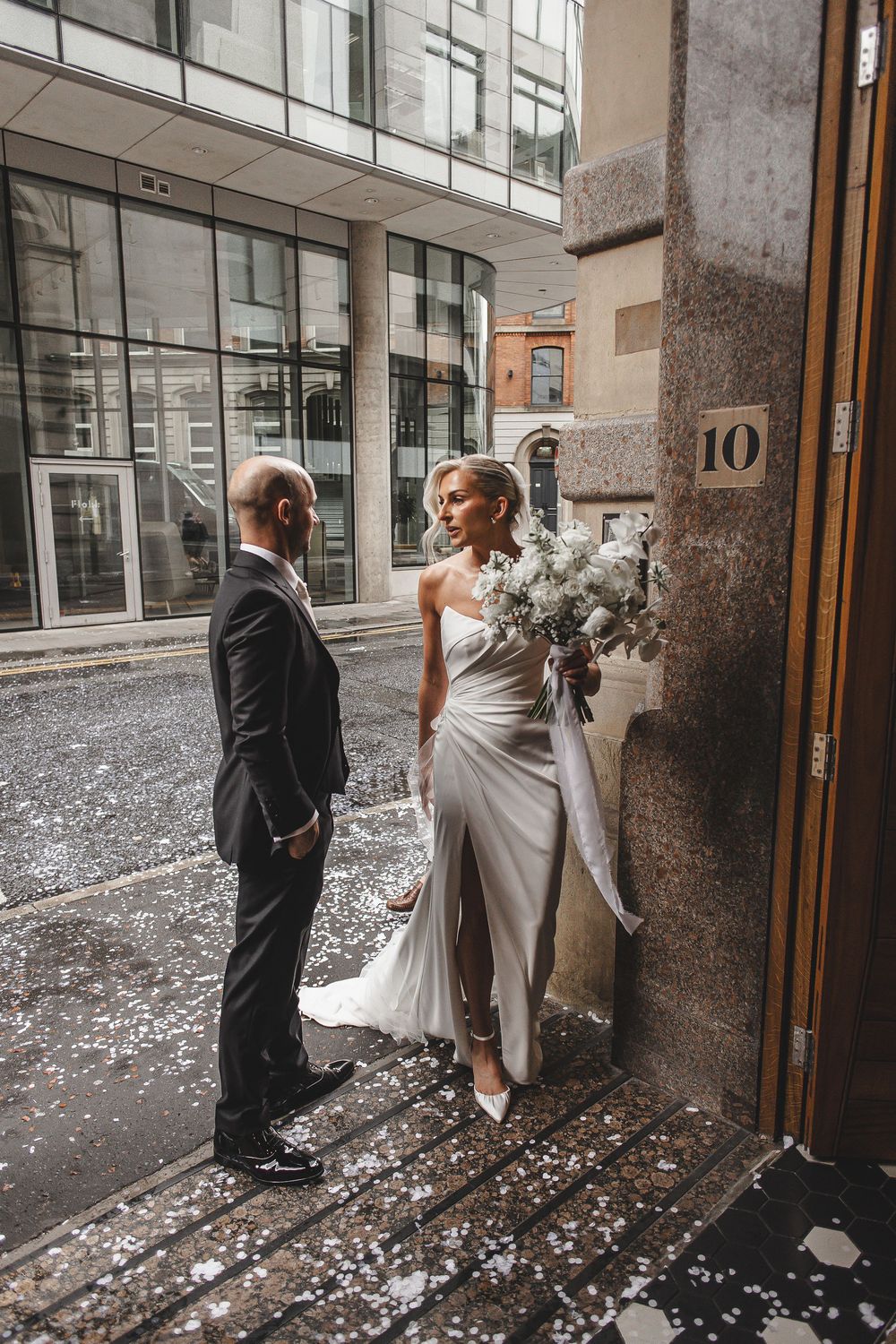 A wedding couple enters a building with white flower petals scattered on the ground in a series of candid shots.