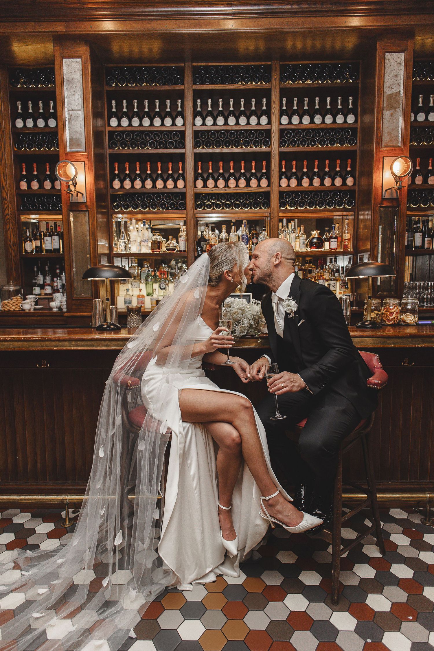 A romantic wedding photoshoot at a vintage bar with wood paneling and bottles lining the walls.