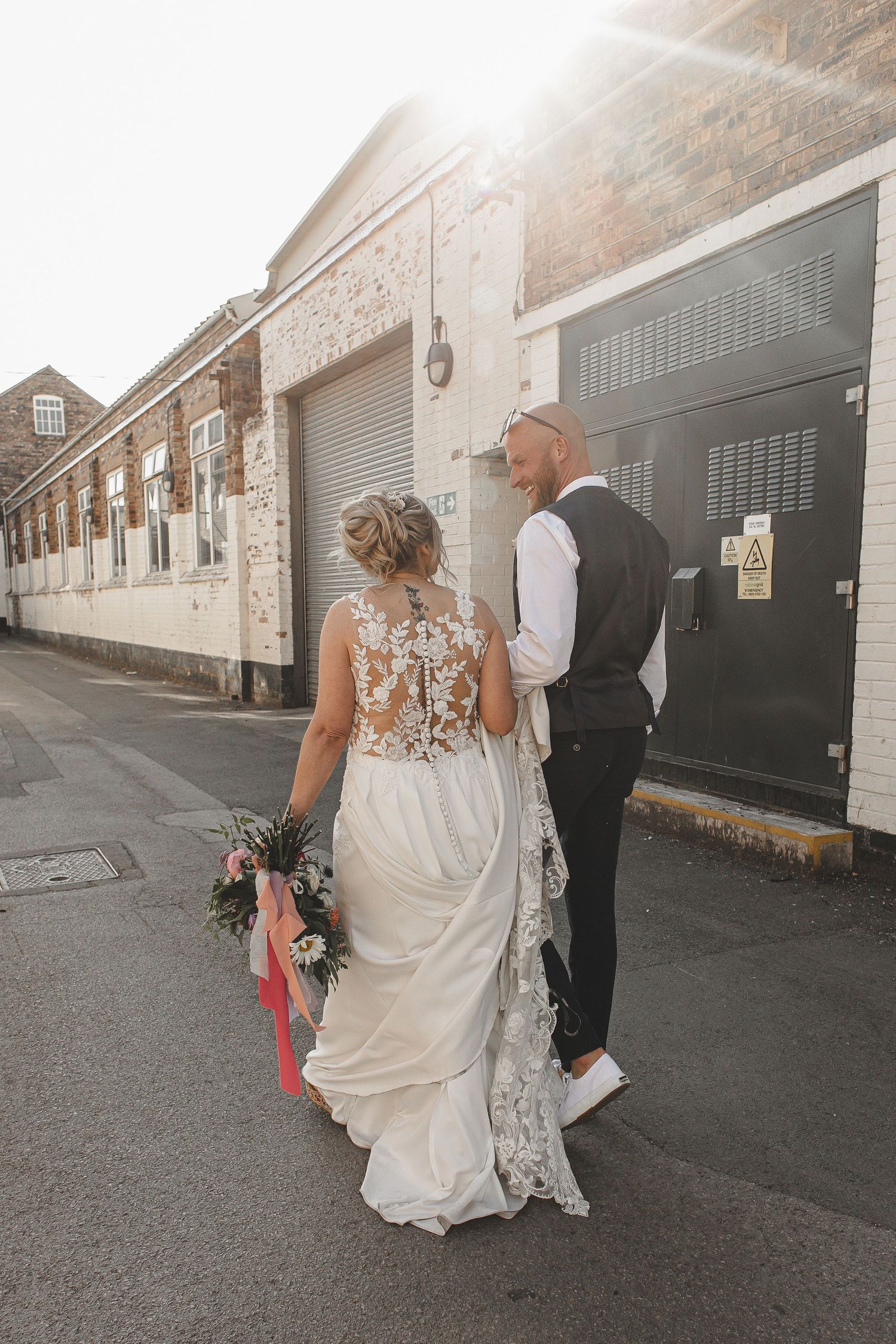 Newlywed couple walks down industrial alley with brick walls and shuttered storefronts on their wedding day.
