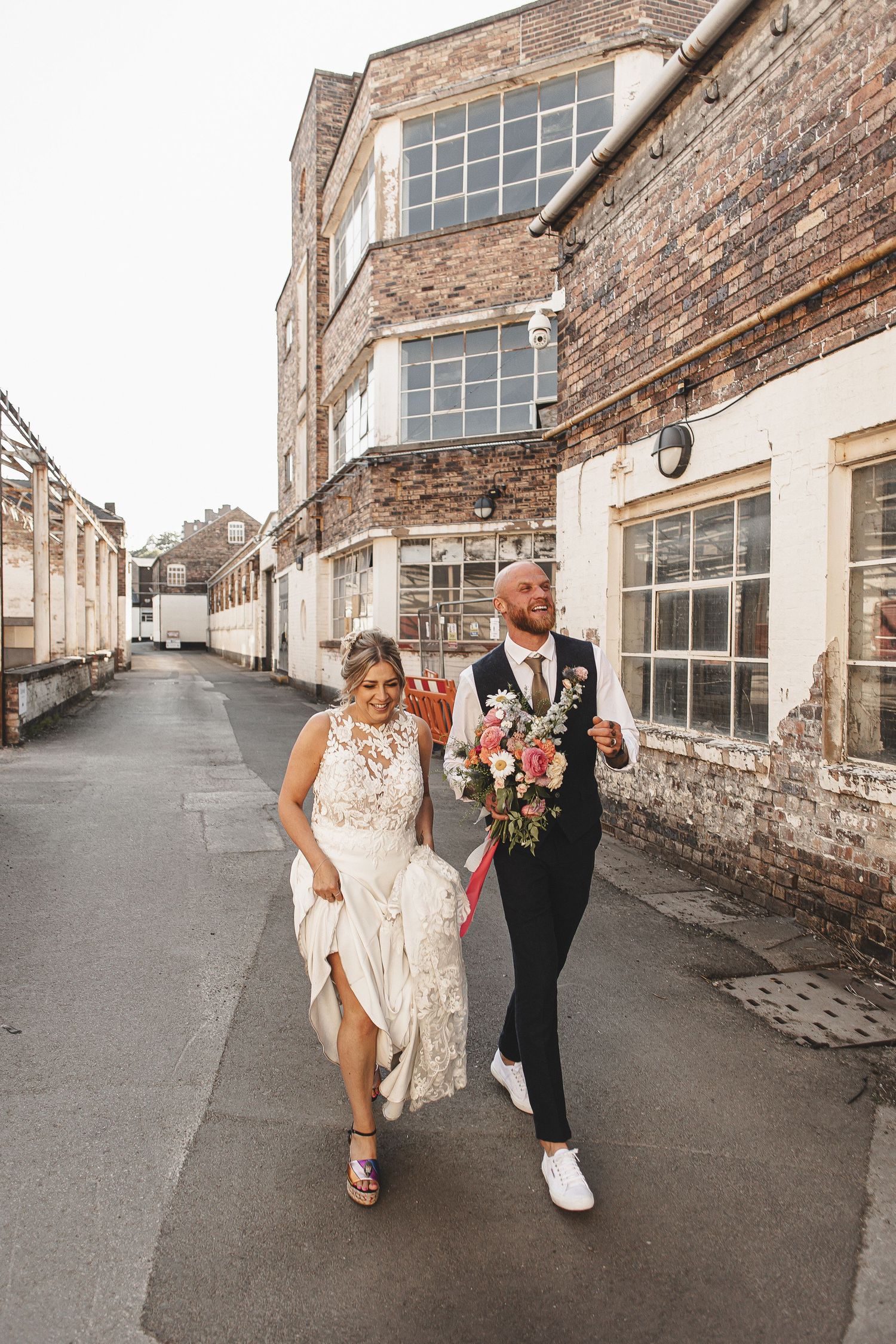 A couple walks together along a rustic brick alley with historic stone buildings on both sides.