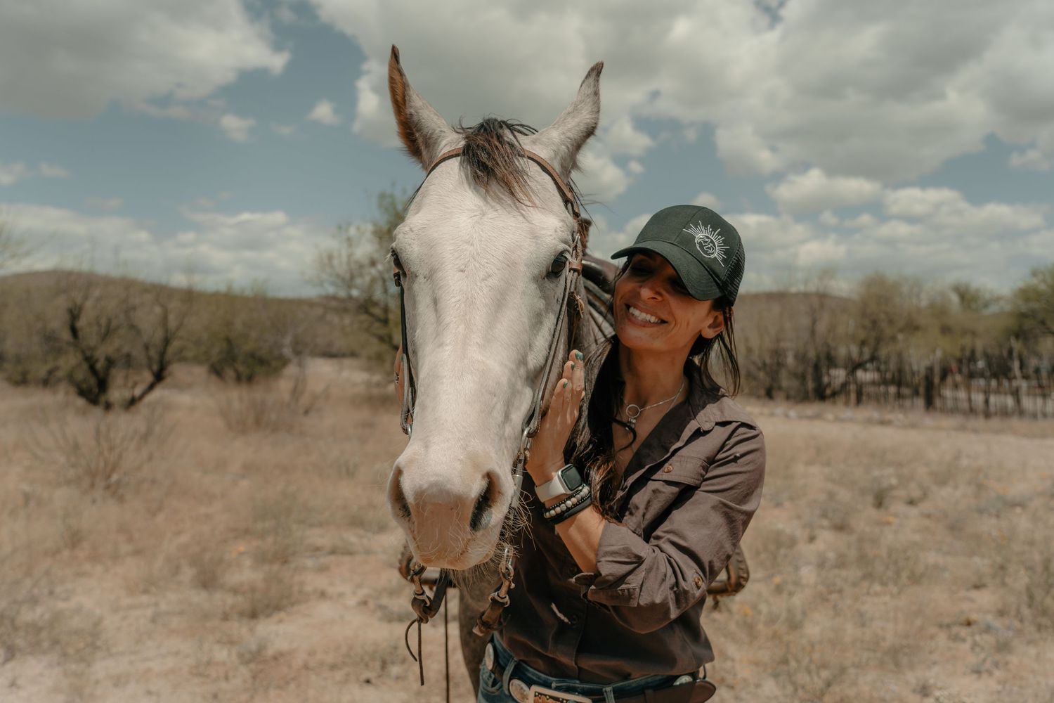 White horse and rider in a cap stand together in a desert landscape.