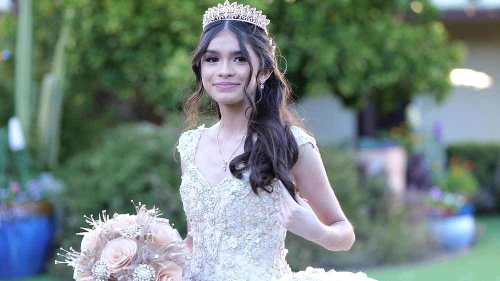 A bride in a white wedding gown and tiara poses in a garden setting during a wedding photoshoot.