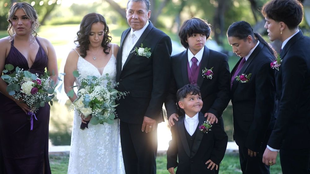 A wedding party poses outdoors in formal attire with purple accents and floral bouquets.