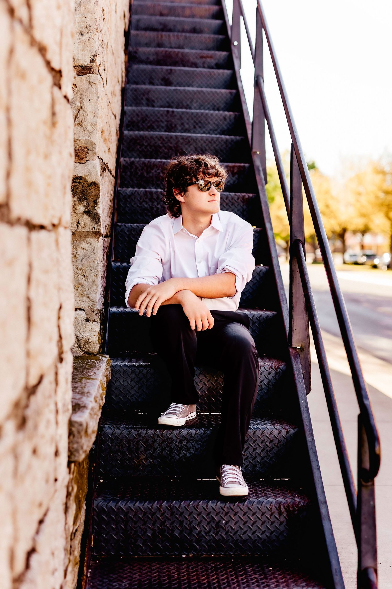 Person in white shirt and sunglasses sitting on metal stairs outdoors.