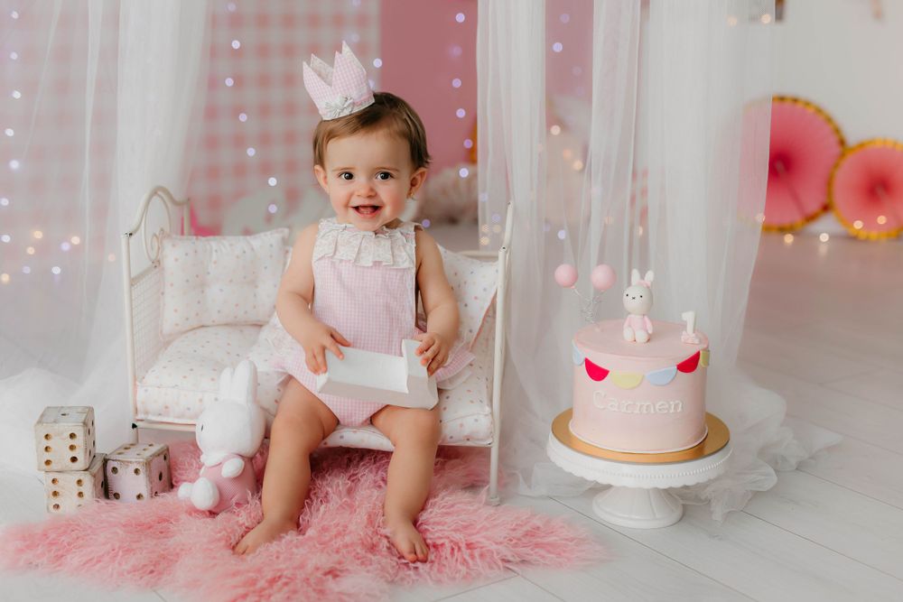 Fotografía del primer cumpleaños de una niña con tarta y decoración en tonos rosas