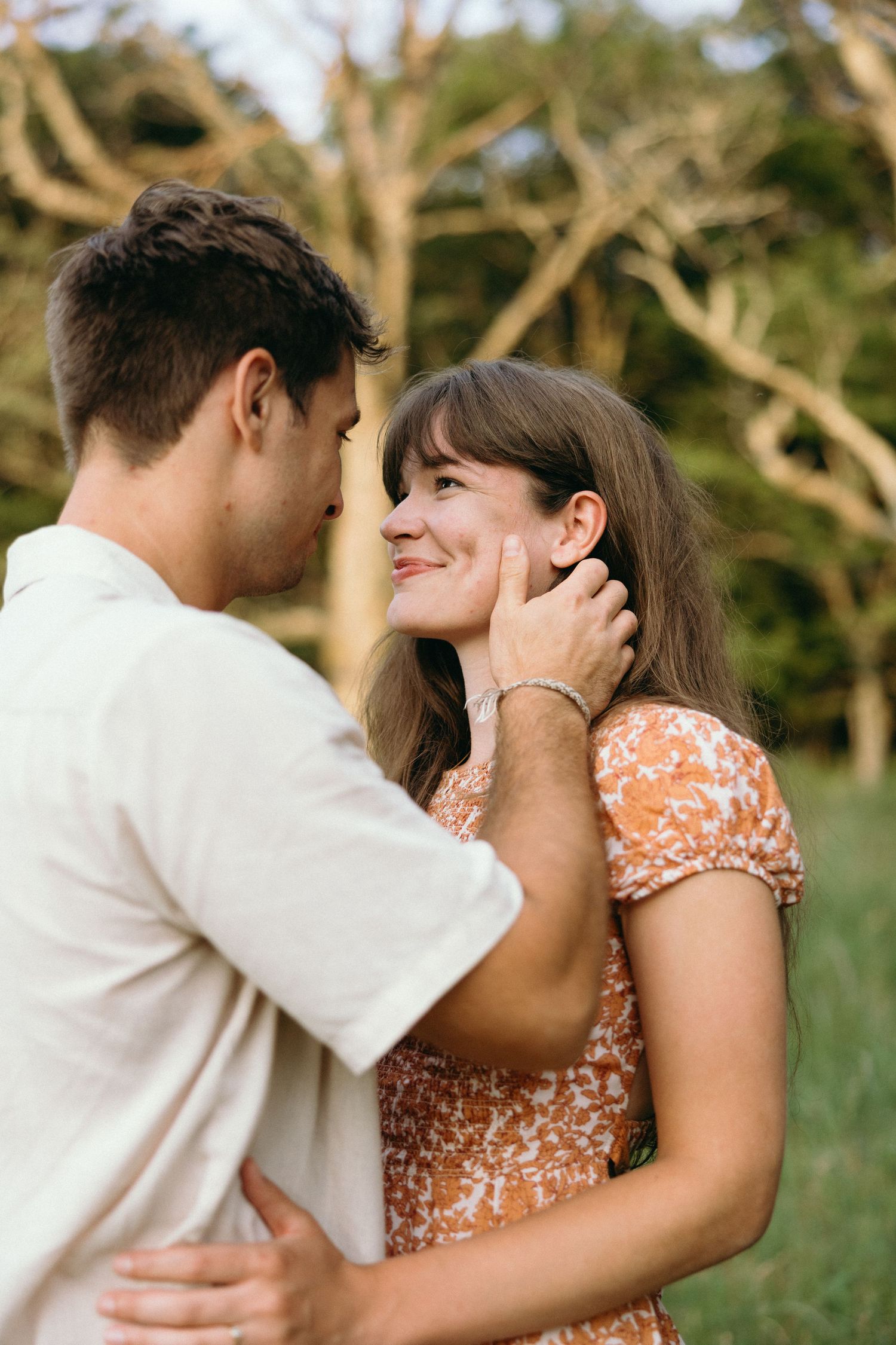 A romantic embrace captured in a sun-drenched field with trees in the background. NC Editorial wedding photographer for historic venue