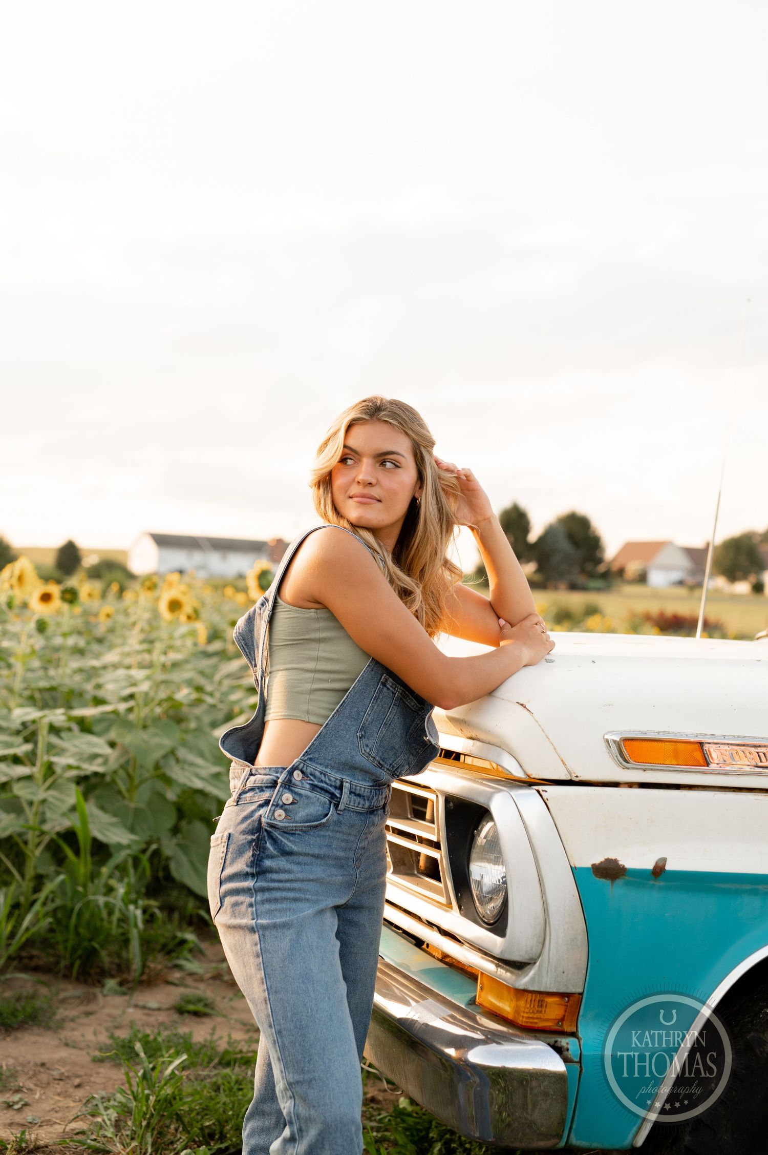 A vintage turquoise truck sits beside a sunflower field during a summer photoshoot at golden hour.