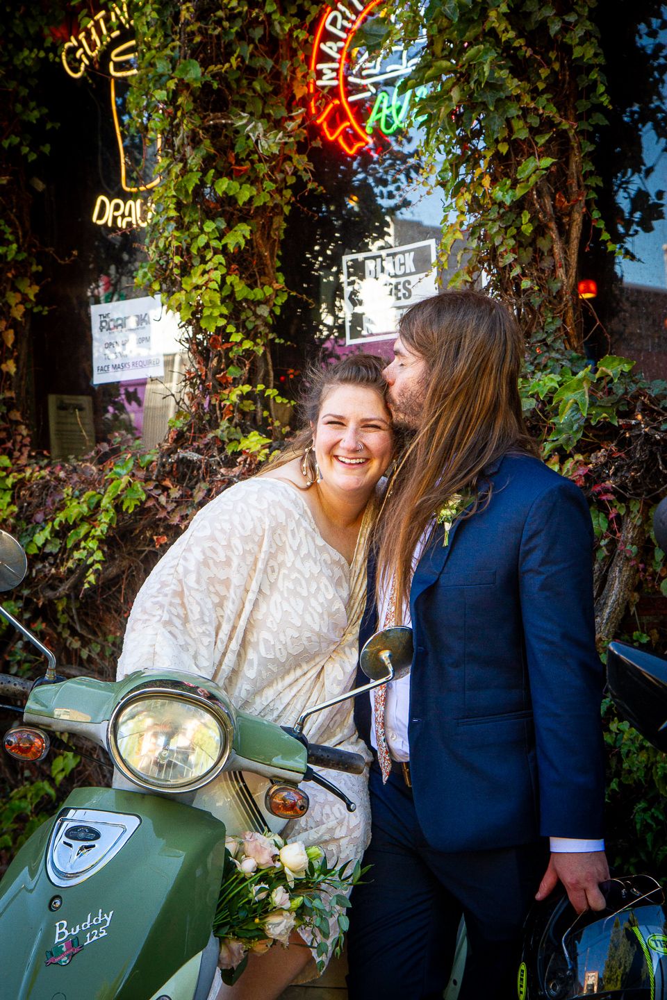 Couple shares intimate moment on vintage scooter with neon lights in background.