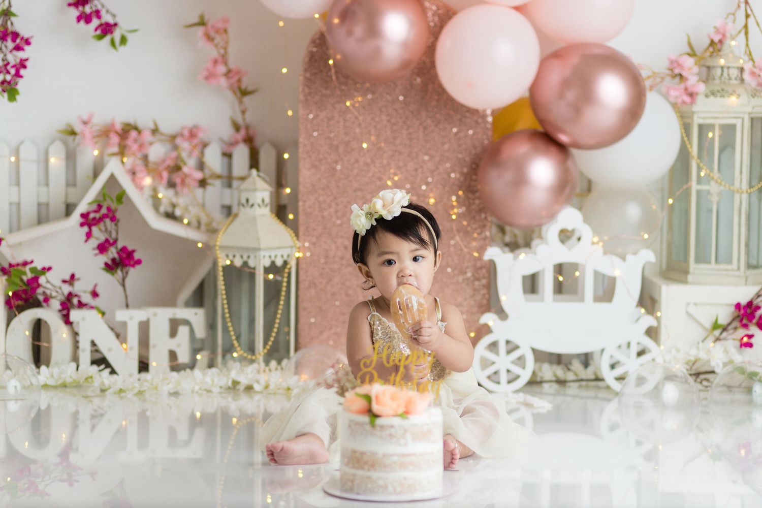 First birthday cake smash setup with rose gold balloons and vintage carriage prop.