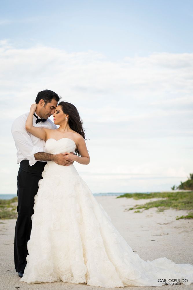 A romantic beach wedding photo showcasing a couple embracing against a bright sky backdrop.