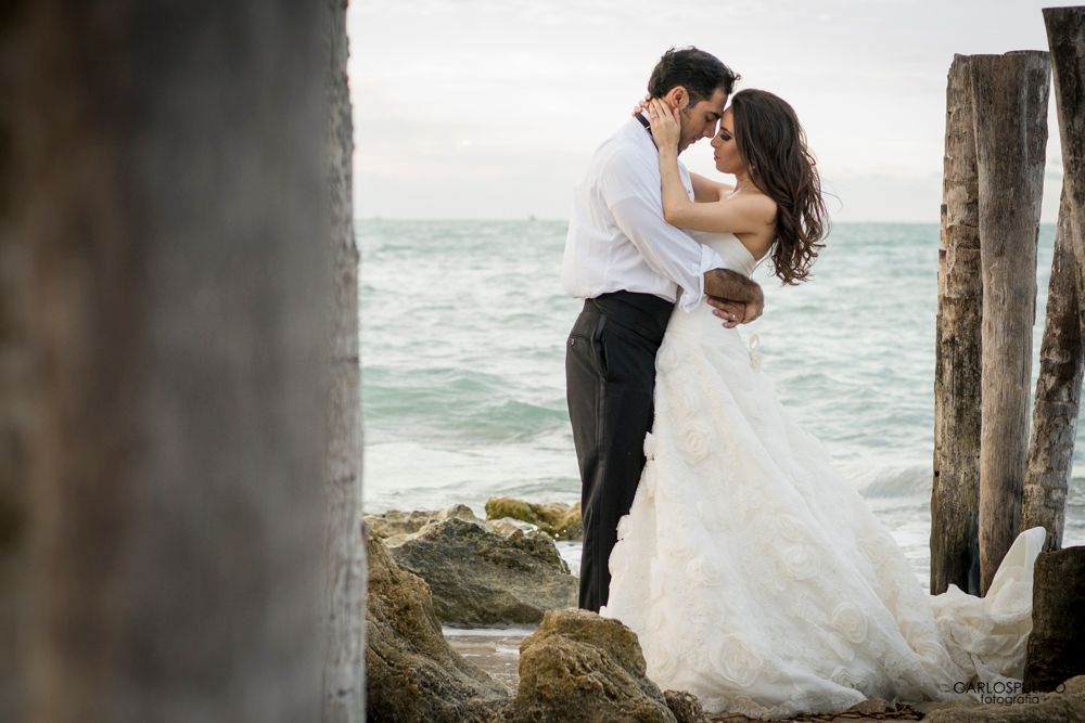 Wedding couple posing romantically among wooden pillars by the ocean.