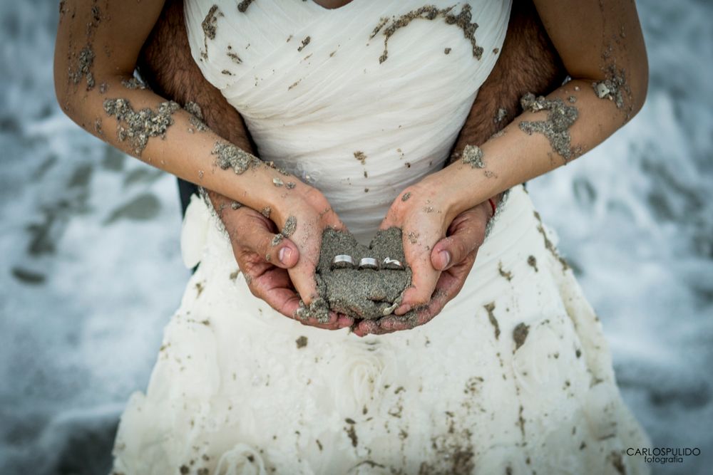 Close-up of hands holding a small object while wearing a muddy wedding dress.