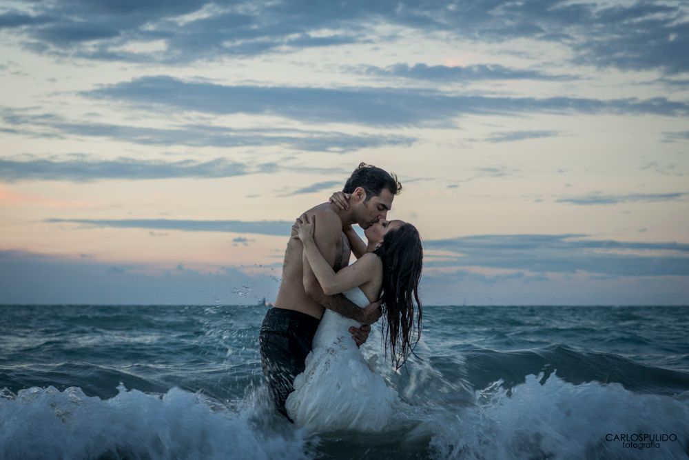 Sunset wedding photo with couple standing in crashing ocean waves.