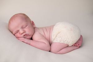 Sleeping newborn baby wrapped in soft cream-colored blanket lying on neutral backdrop in professional studio setting.