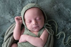 Newborn baby in a green romper with matching bonnet sleeping