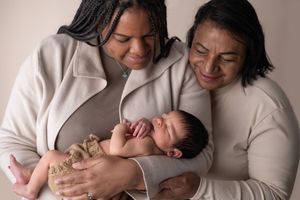Mother and daughter embrace whilst holding the dauhter's newborn baby.