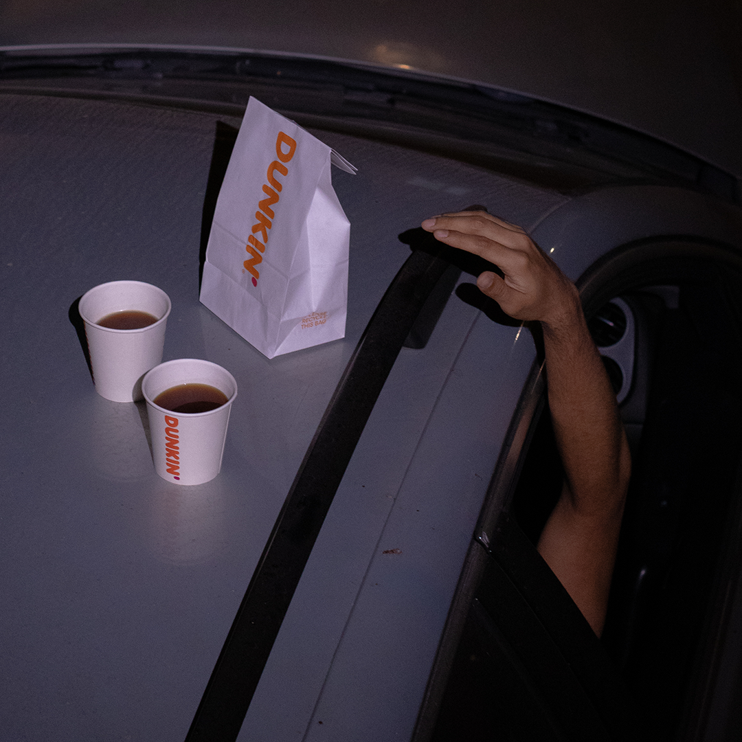 Dunkin' Donuts cups and bag on a car dashboard at night.