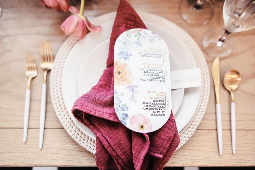 Wedding table place settings with burgundy napkins and white plates on wooden surface.