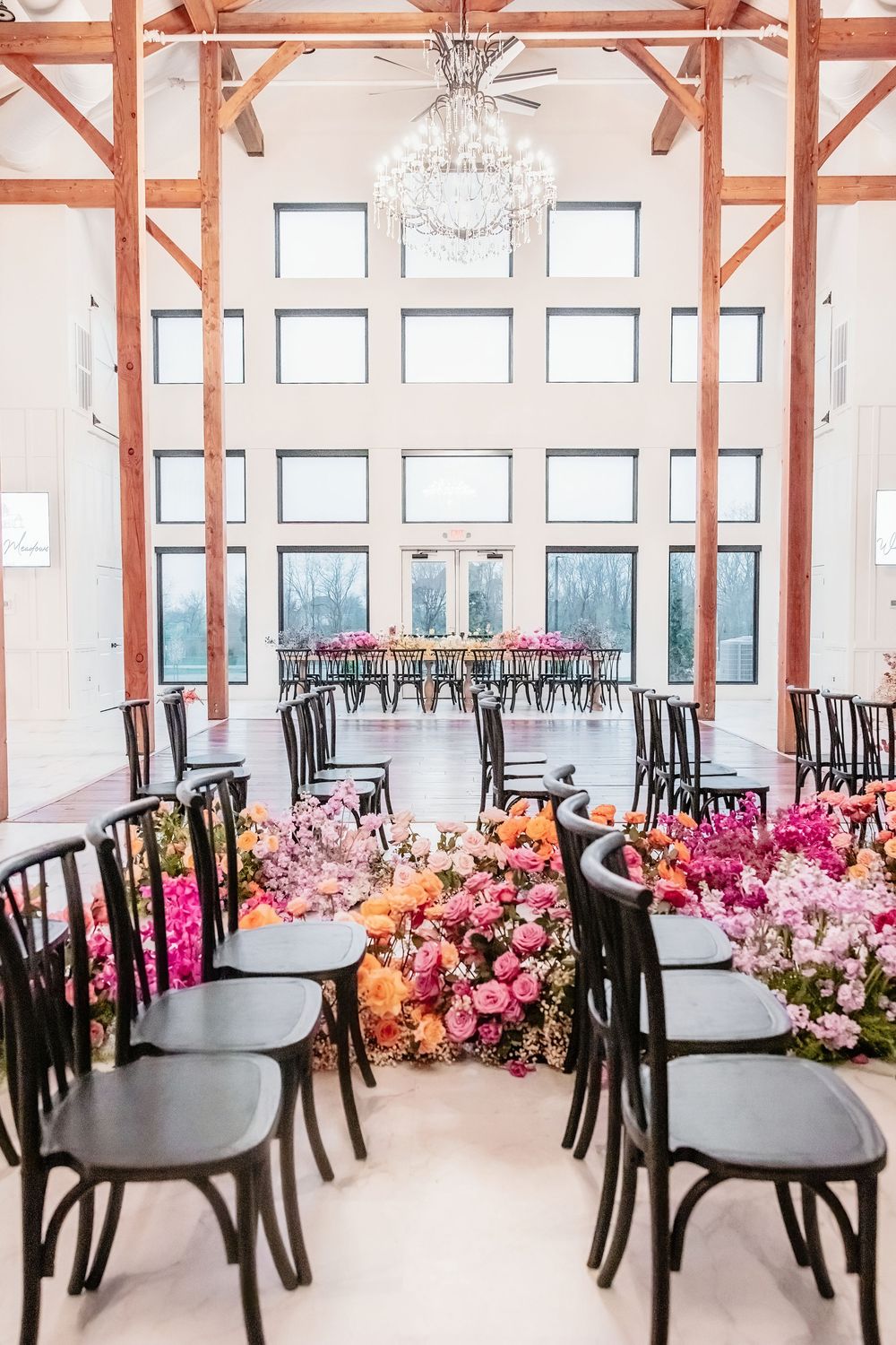 Modern event venue with black chairs and vibrant pink floral arrangements along windows in an elegant indoor setting. White Willow Meadows