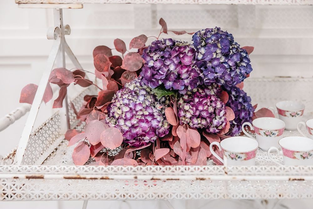 Purple hydrangeas and pink eucalyptus leaves arranged on a white vintage surface with decorative elements.