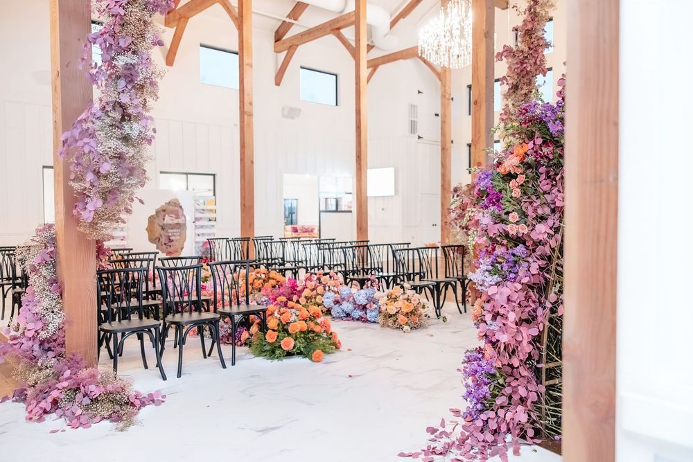Wedding venue space decorated with purple floral arches and black bistro chairs.