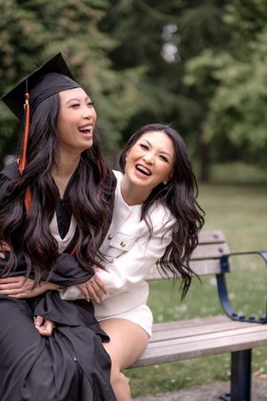 Graduation photoshoot in a park with joyful laughter and casual poses on a wooden bench.