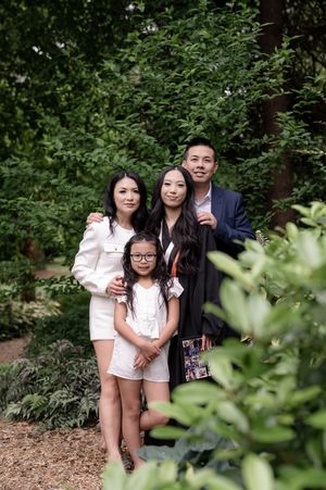 A group poses together outdoors in a garden setting with lush green foliage in the background.