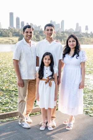 Family of four in white outfits posing on a dock with a city skyline and lily pad lake in the background.