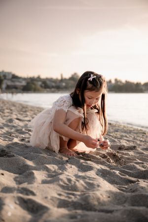 Child in tulle dress crouches to play in the sand on a sunset beach.