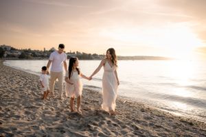 Family walks hand in hand along sandy beach during golden hour sunset.