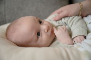 Close-up of infant lying down with curious expression and wearing light colored outfit.