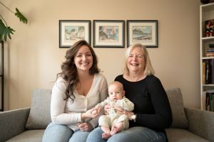 Three generations share a happy moment together on grey couch with decorative wall art.