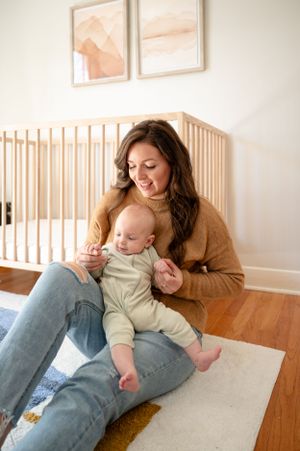 Candid moment of parent and baby relaxing together on floor near wooden crib.