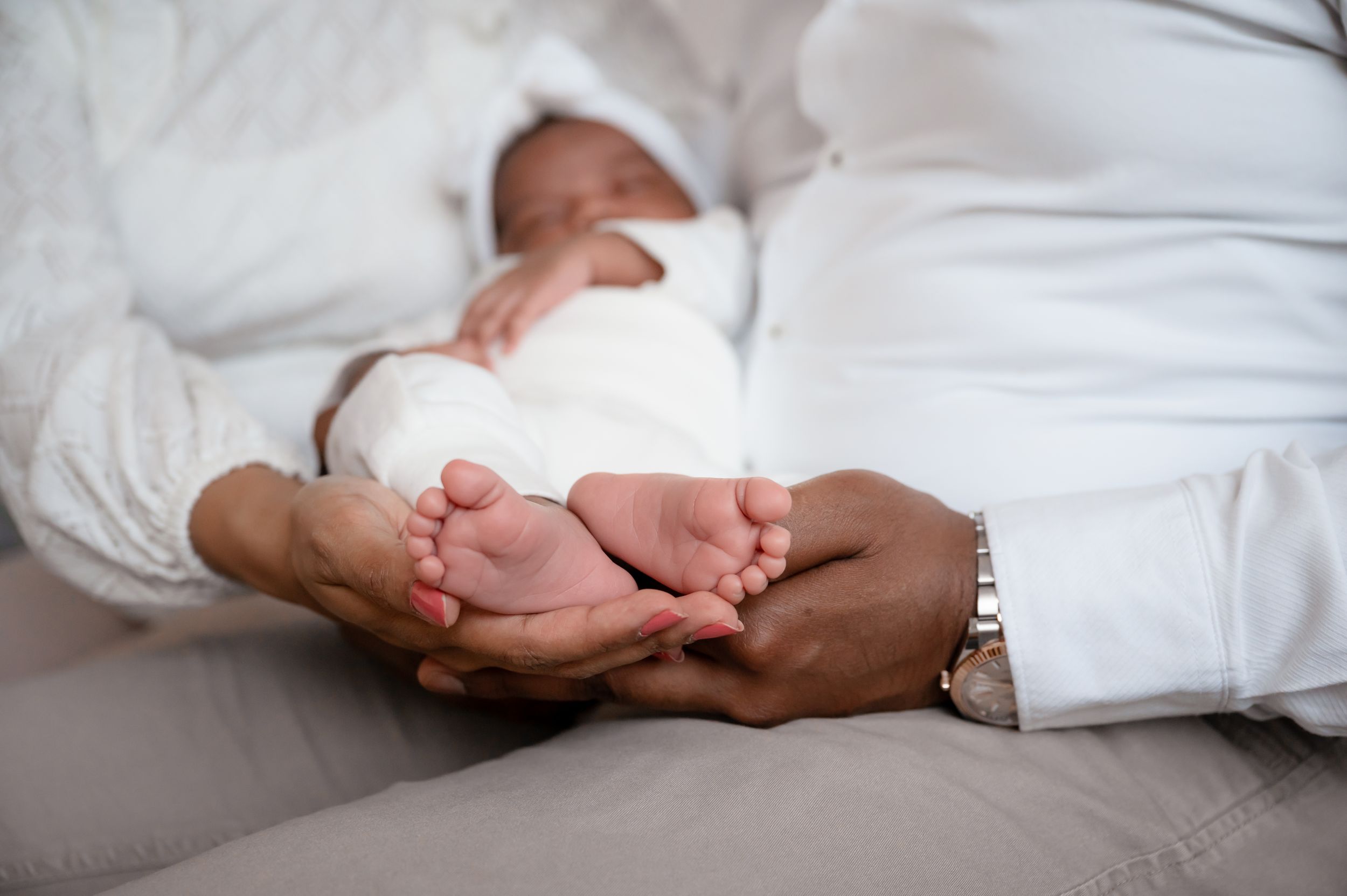 Close-up of tiny baby feet being held in adult hands on white bedding.