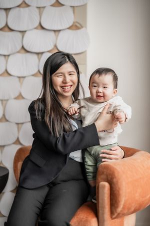 Woman in black business attire sits on orange armchair with laughing baby in light colored outfit.