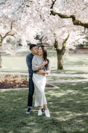 A couple embraces under blooming cherry blossom trees on a spring day in a grassy park.