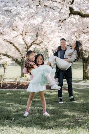 A family enjoys a playful moment under blooming cherry blossom trees on a spring day in the park.
