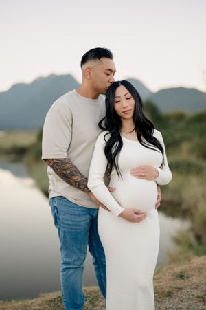 Expecting couple poses together in white dress and casual wear during sunset maternity photoshoot in desert landscape.