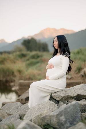 A white-clad figure poses gracefully on rocky terrain against a mountain landscape at sunset.