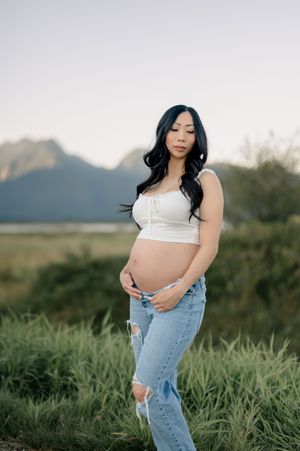 A serene outdoor photoshoot in tall grass features someone wearing a white crop top and distressed denim jeans.