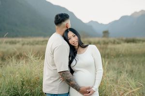 A couple embraces in a grassy field with misty mountains in the background during a romantic outdoor photoshoot.